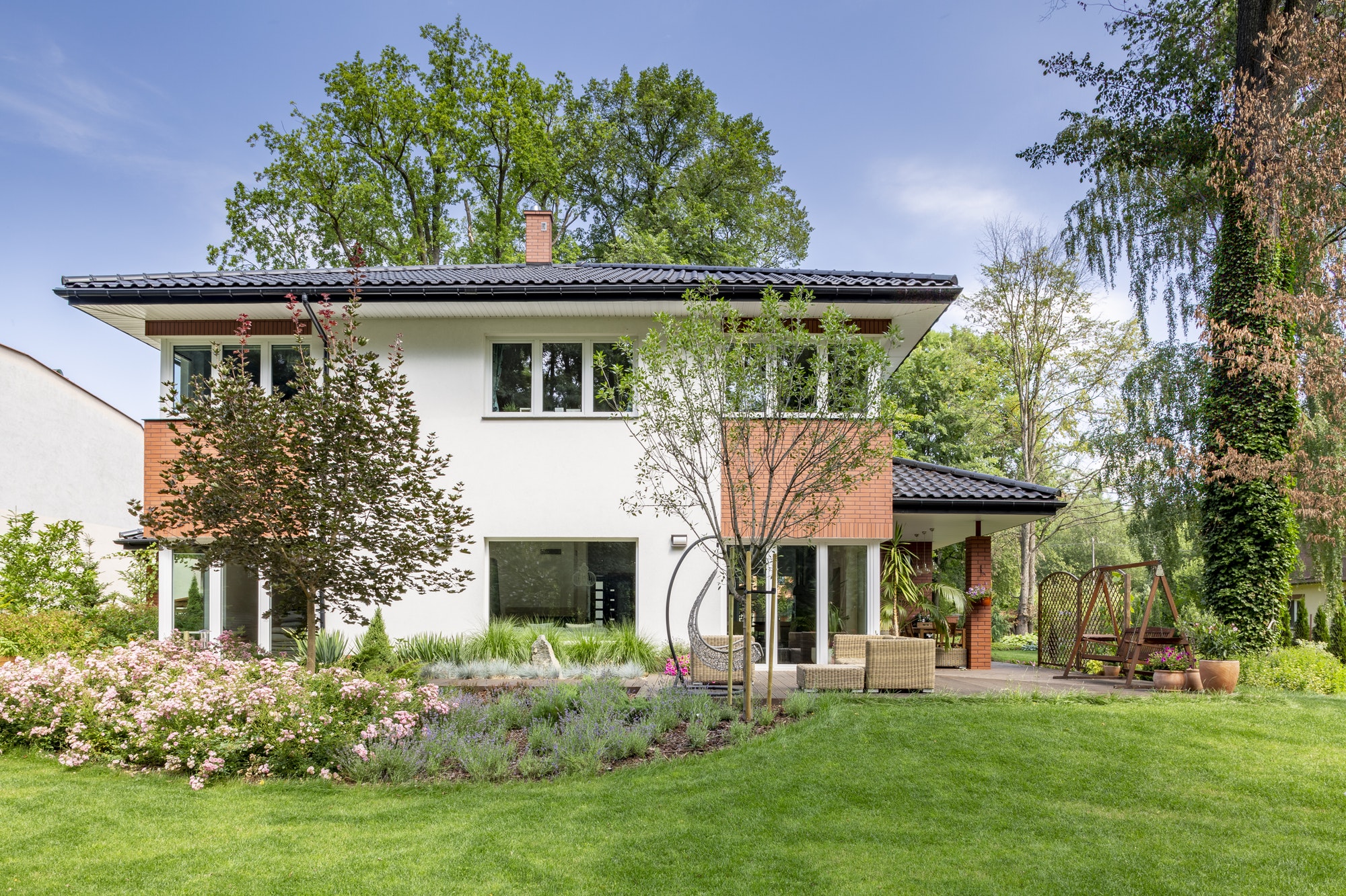 Flowers and trees in the garden of white house with windows duri