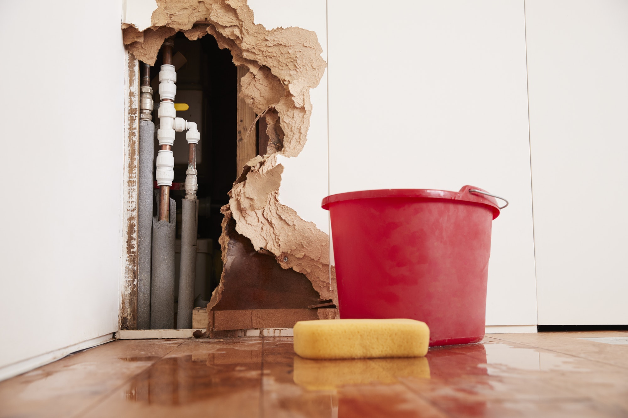 Damaged wall, exposed burst water pipes, sponge and bucket